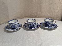 Three full sets of Royal Crown Derby Mikado cups and saucers arranged in a row on a white surface, showing their overall shape, pattern and size.