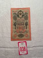 Front side of the 1909 Russian 10 Ruble banknote on a white fabric background with a lot tag number 038 visible.