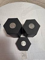Three black hexagonal coin holders displaying 1971, 1982, 1984 Canadian dollars on top surfaces.