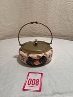 Front view of vintage round ceramic jar with floral design, brass-toned EPNS lid and handle.