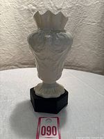 Full view of the Belleek porcelain vase showing its shape, contours, and base on a black stand with lot number card in front.