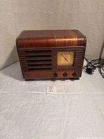 Front view of wooden case vintage radio with power cord, showing control knobs and tuning dial on front.