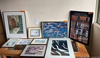 Photo showing all nine assorted framed and unframed art pieces arranged on a table and leaned against the wall.