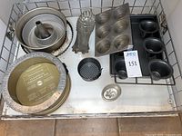 Top view of multiple baking pans including springform pans, cupcake trays, tart pans, funnel pan and pie crust shield in a metal basket.