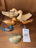 Photo showing four carved wooden ducks, one carved songbird on stand, and one vintage brass quail figurine arranged on a wooden surface.