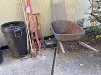 Wide view showing wheelbarrow, garbage can, and assorted garden tools leaning against wall
