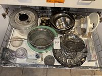 Wide view of the assortment including mixing bowls, strainers, salad spinner, grater, citrus juicer, and garlic baker.