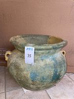 Side view of faux ceramic planter showing rounded bulbous shape, painted muted blue-green-gold finish, two handles, and drainage hole.