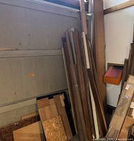 Photo of vertical stack of various long wood planks and boards leaning against wall and garage door, some pieces with rough edges and some finished.