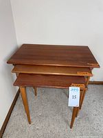 Angled front view of three nested tables showing teak tops and tapered legs