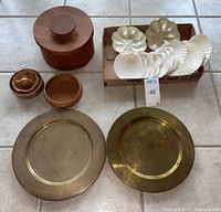 Overview of all wooden serving bowls, teak canister, brass chargers and shell dishes on tile floor.