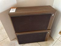 Pair of vintage AR speakers with wood veneer cabinets stacked on a tile floor, black fabric fronts with AR logo.
