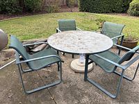 Full lot view showing round glass-top table, four mesh chairs, umbrella and base