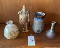 Four assorted pottery vessels including a jug, three-sided vase, wide-mouth vase, and small vase on wood surface