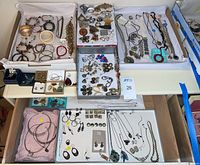 Top-down view of multiple trays showing assorted necklaces, bracelets, earrings, cuffs, pins and pendants