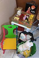 Wide shot showing multi-colored vintage child's rocking chair, toy storage cube with assorted vintage toys, Barbie case, and storage bin of stuffed animals