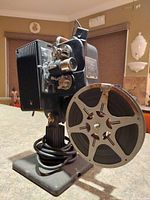 Side view showing the film projector body, reel, base, and electrical cord wound on base