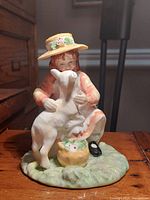 Front view of the Royal Doulton figurine showing the girl holding the white goat sitting on green base.