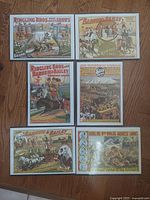 Top-down view of six colorful circus posters placed on wooden floor, showing title and imagery for Ringling Bros., Barnum & Bailey, and Sells Brothers circuses.