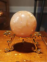 Flower Agate sphere on gold stand showing front and side views with light reflection and visible internal floral inclusions.