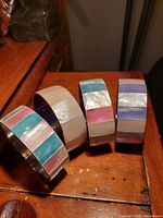 Four handmade Filipino stainless steel and mother of pearl bangles arranged in a row on a wooden surface, showing colorful inlaid segments.