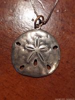 Close-up photo of silver sand dollar pendant with engraved starfish design and holes