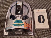 Packaged Nano Audio wireless neckband headphones and sealed Monkey Smart Band fitness watch box on carpeted floor.