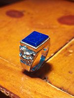Ring standing on wooden surface showing polished rectangular lapis lazuli stone on top and detailed stallion design on one side of the band.