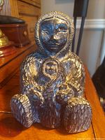 Front view of the sculpture showing the mother figure holding the child, highlighting the facial details and textured body surface.