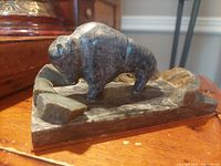Side angled view of the stone buffalo sculpture on a wooden surface showing the buffalo figure and textured base details.