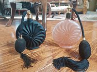 Two vintage art glass perfume atomizers displayed on a hardwood floor, featuring spiral designs and fabric bulbs.