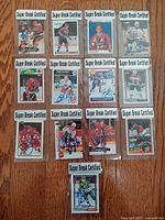 Photo showing all thirteen vintage autographed NHL player cards with Super Break Certified label in protective sleeves spread on wooden floor.