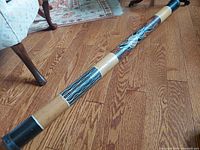 Full view of the rain stick showcasing painted designs and bamboo material on wood floor.