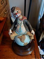 Front view of vintage hand painted clown sitting on a globe on a wood music box base.