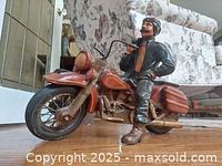 Front right angled view of the handcrafted folk art motorcycle rider figurine sitting on red motorcycle, showcasing detailed motorcycle front and rider's pose.