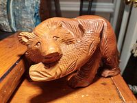 Front angle showing brown bear holding a salmon carved from wood with detailed textured fur and scales on the fish.