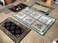 Four area rugs laid out on carpeted floor, showing variety of colors and designs including floral and geometric patterns