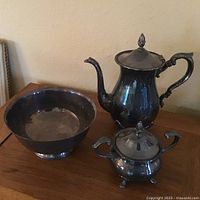 Photo showing a dark stainless steel coffee pot with lid and handle, a sugar bowl with lid and two handles, and a round serving bowl.