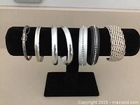 Photo of 7 costume jewelry bangles displayed on black bracelet holder stand, showing various designs and colors.