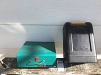 Front view of green metal box camp stove and black propane lantern case