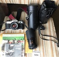 Overall photo showing Canon AE-1 camera with 50mm FD lens, telephoto FD lens, carrying cases, manuals, and camera strap on a striped chair.