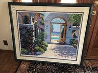 Framed art print "Hotel California" by Howard Behrens featuring garden architecture with ocean view, displayed against wooden cabinet.