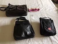 View of all items in the lot including handbags, bath kit, cosmetic bag, and fabric accessory laid out on a light surface.