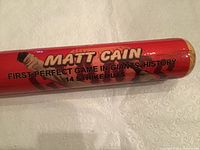 Close-up photo of the baseball bat with the text 'MATT CAIN', 'FIRST PERFECT GAME IN GIANTS HISTORY 14 STRIKEOUTS' clearly visible.