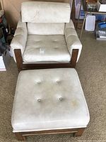 Front view of mid-century modern side chair with ottoman showing cream Naugahyde upholstery with button tufting and wood frames.