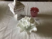 White milk glass basket with deep ruffled edges holding three horn-shaped vases with hobnail texture and ruffled rims, displayed on a light patterned tablecloth.