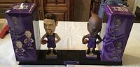 Two Sacramento Kings bobblehead figures representing Bobby Jackson and Scott Pollard, both on stands with their original boxes shown behind them on a table.