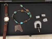 Display of all items included in the lot showing watch, necklace pendant, and silver belt buckle set