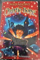Cover of the book 'Midnight for Charlie Bone' by Jenny Nimmo showing a boy with a glowing book, magical elements and dark background.
