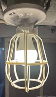 Close-up of one white ceiling light bulb cage cover with a bulb inside, mounted upside down on a ceiling with white round fixture base.